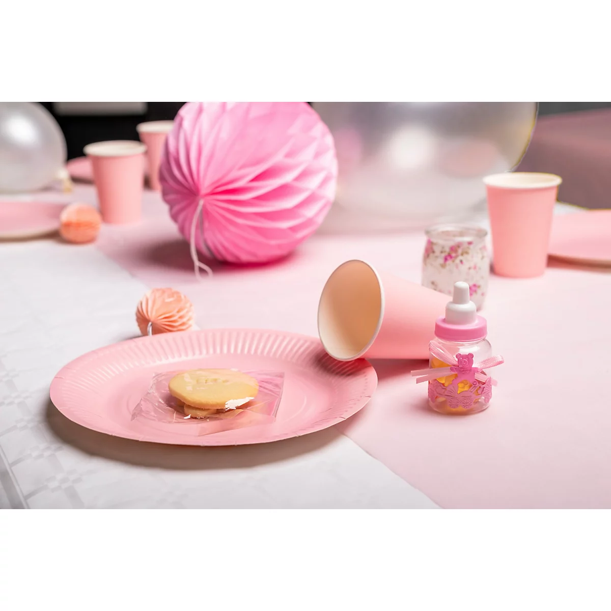 Ein Tisch ist für eine Babyparty in Pink dekoriert. Teller, Becher, Kuchen, eine Babyflasche und ein Papierball.