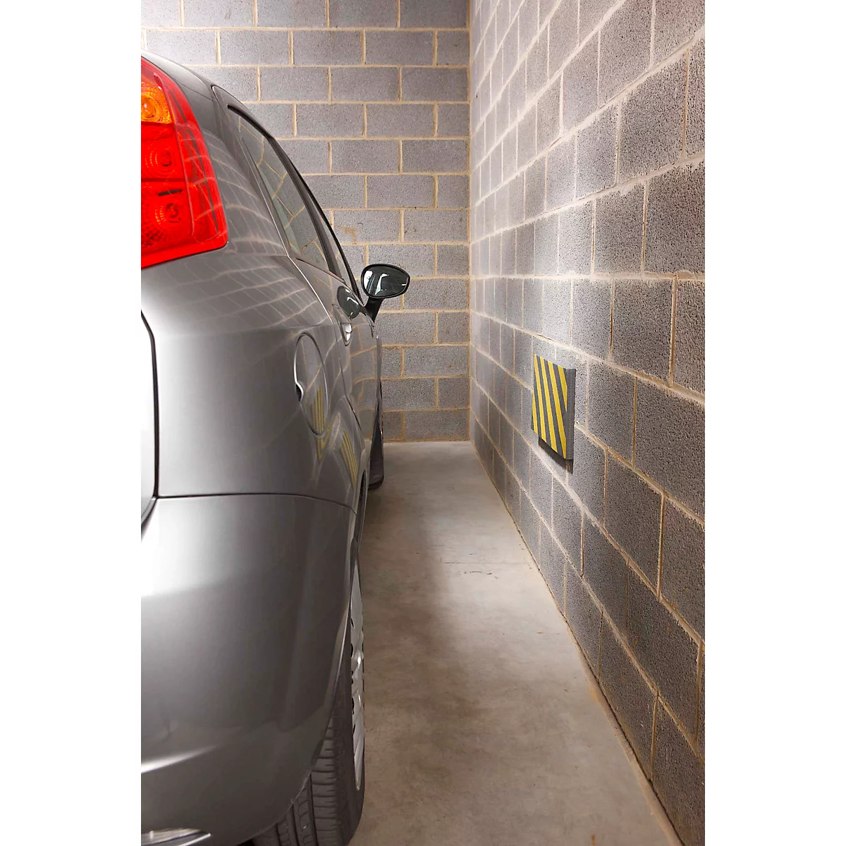 Voiture grise dans un garage étroit, mur avec protection jaune et noire.