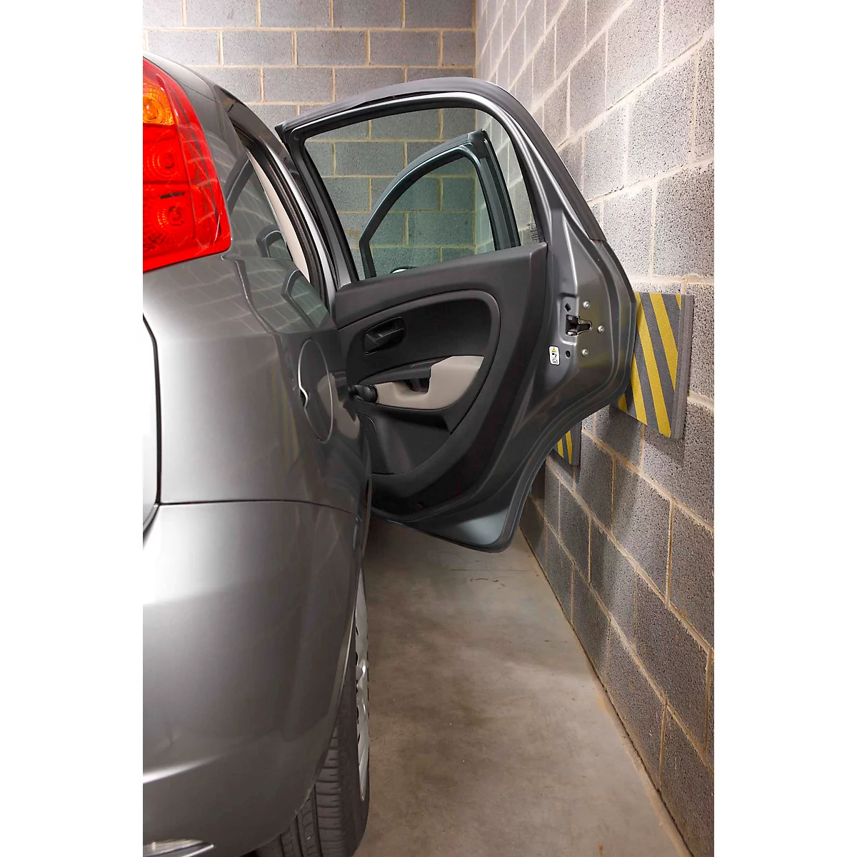 Voiture grise avec portière ouverte à côté d'un mur en briques. Rembourrage mural jaune et noir.