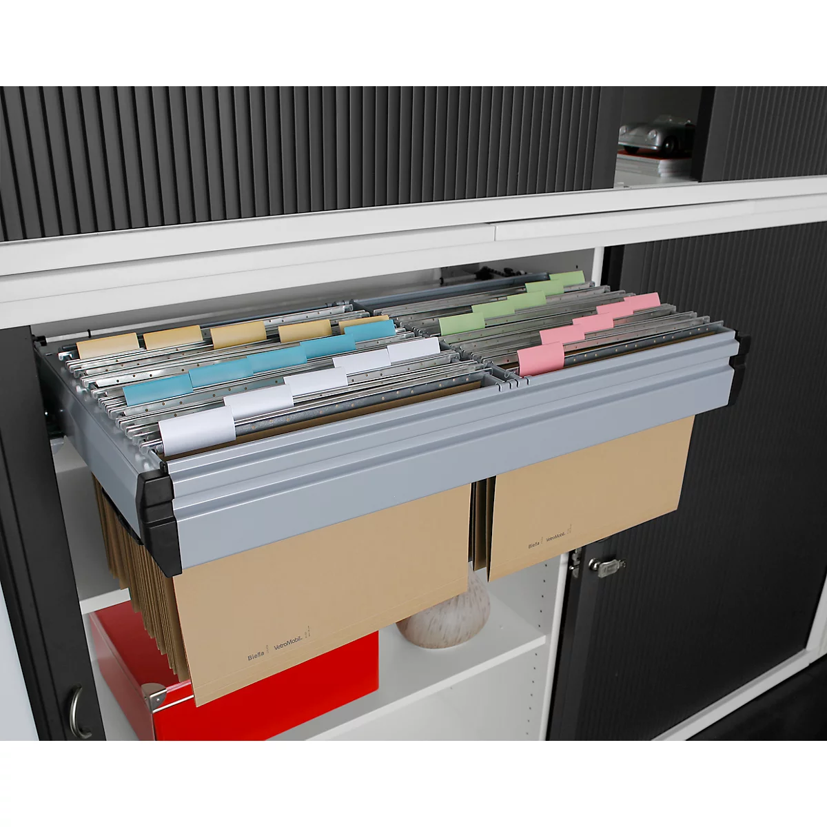 Open file cabinet with colored index cards, beige and red folders in the lower part. Gray cabinet doors.