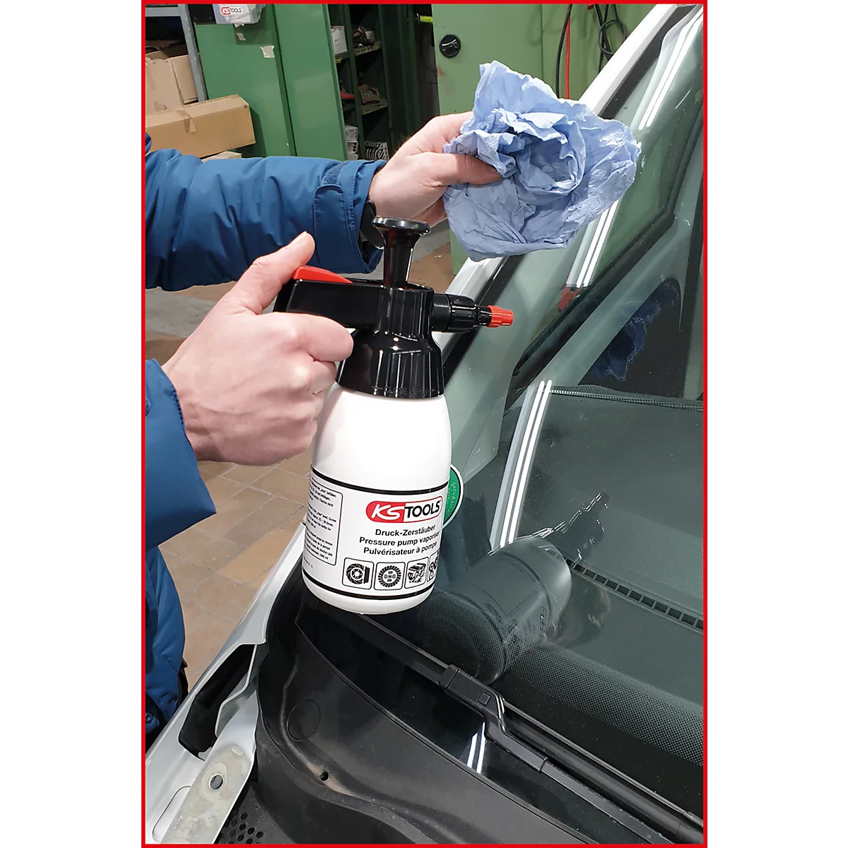 Person reinigt Autoscheibe mit Drucksprüher, Halterung KS TOOLS, blauem Tuch.
