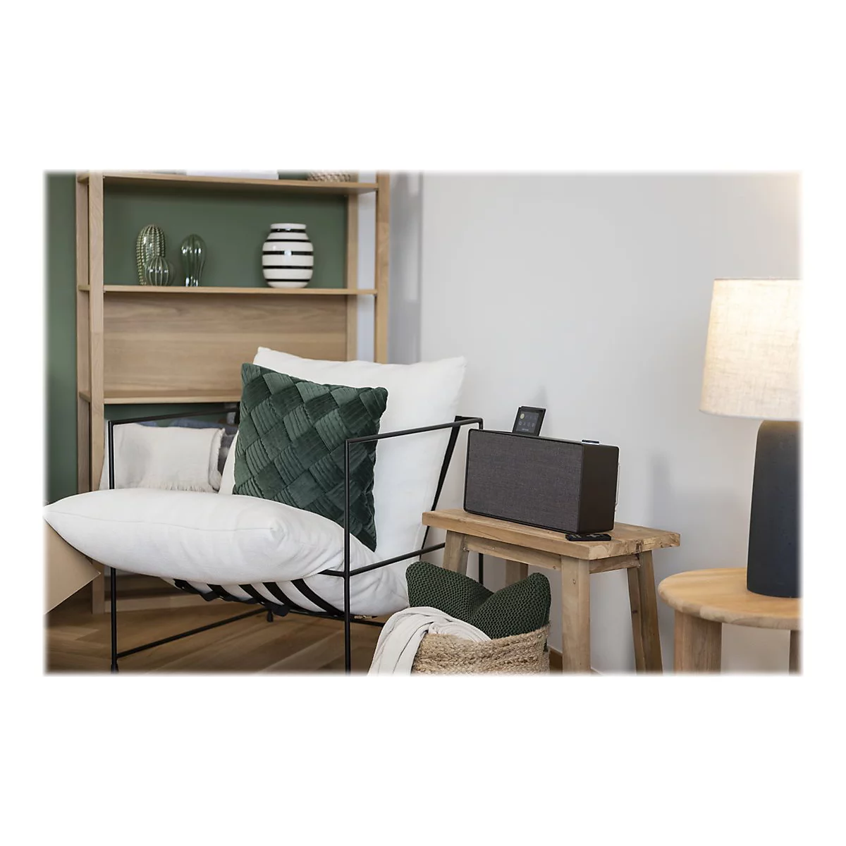Ein Wohnzimmer mit einem Lautsprecher, einem Stuhl mit Kissen, einer Lampe und Dekorationsgegenständen.