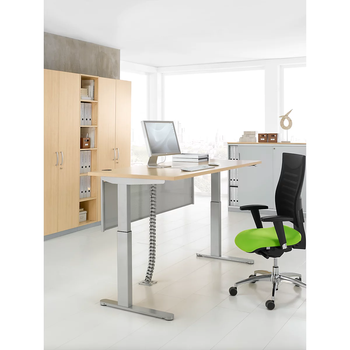 Bright office desk with silver legs, monitor and chair. Cabinet and window in the background.