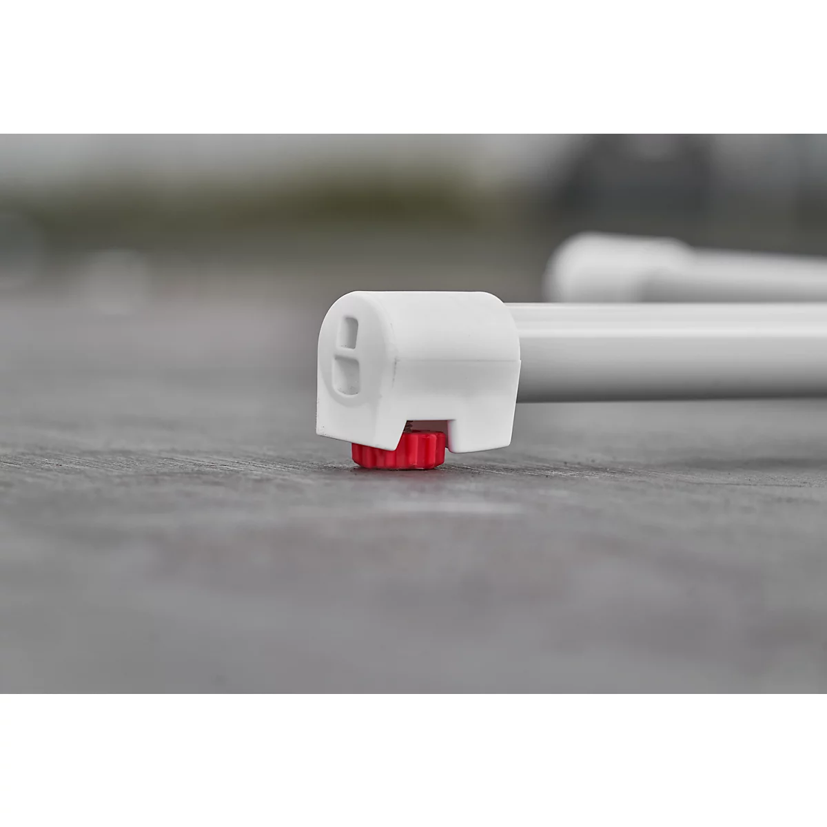 Close-up of a white plastic part with a red screw. The background is blurred.