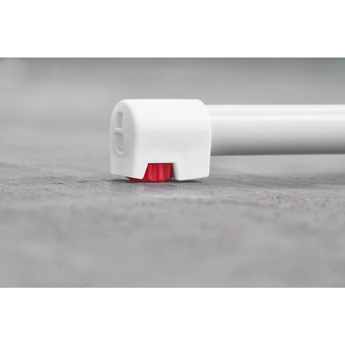 Close-up of the end of a white tube resting on a gray surface. A red knob is visible.