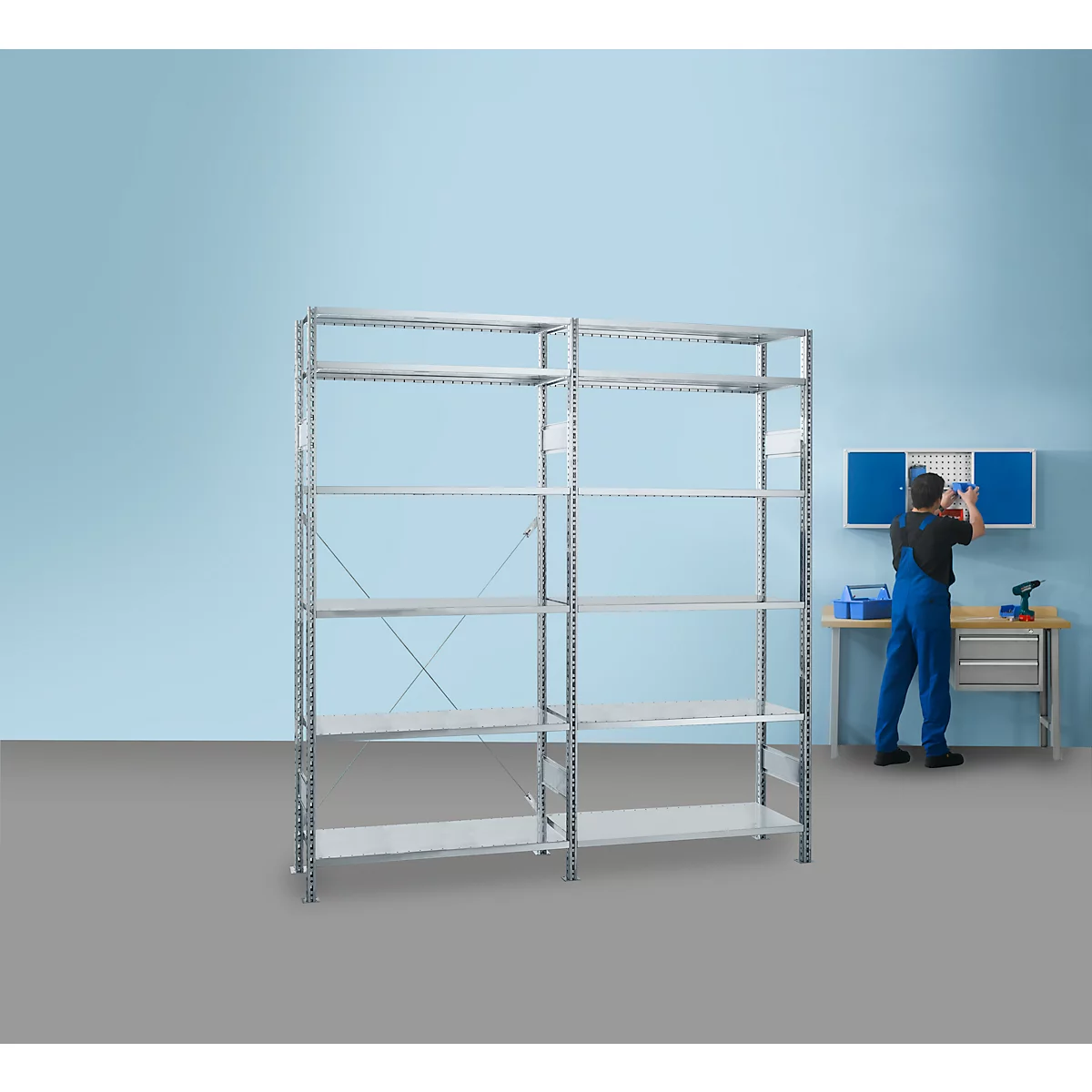 A man is assembling a shelf in a workshop. The shelves are in front of a blue wall. On the right, a man in blue overalls.