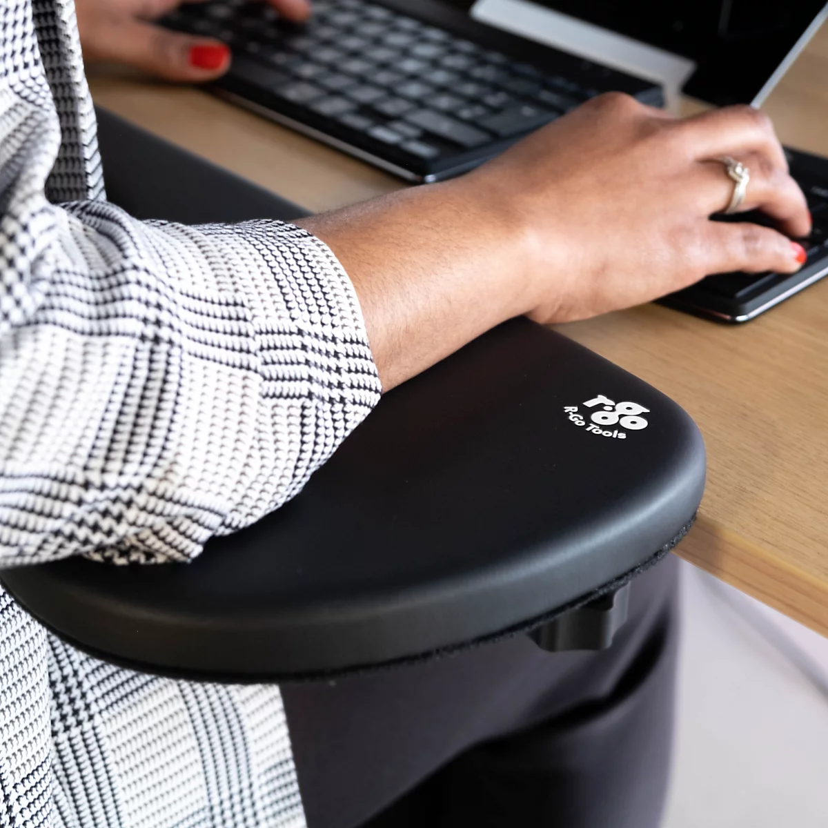 Close-up of a person working at a black desk, with an arm rest supporting the arm.