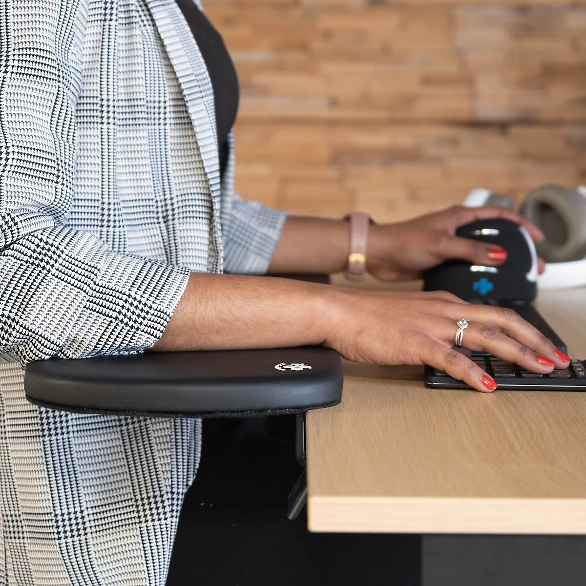 Person working with a black elbow cushion and ergonomic mouse. She is wearing a blazer.
