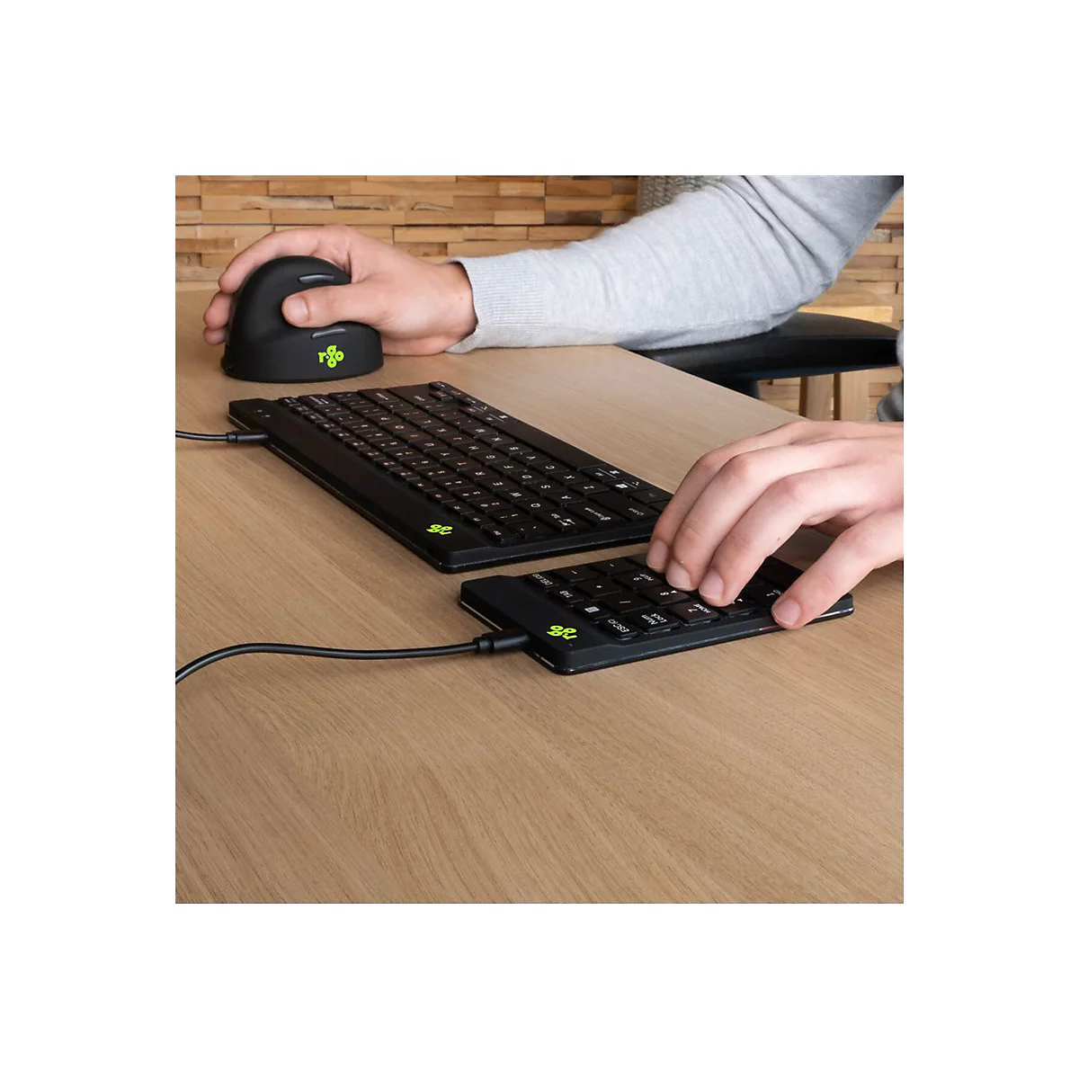 Person verwendet eine ergonomische Vertikalmaus und eine geteilte, kompakte Tastatur an einem Holztisch.