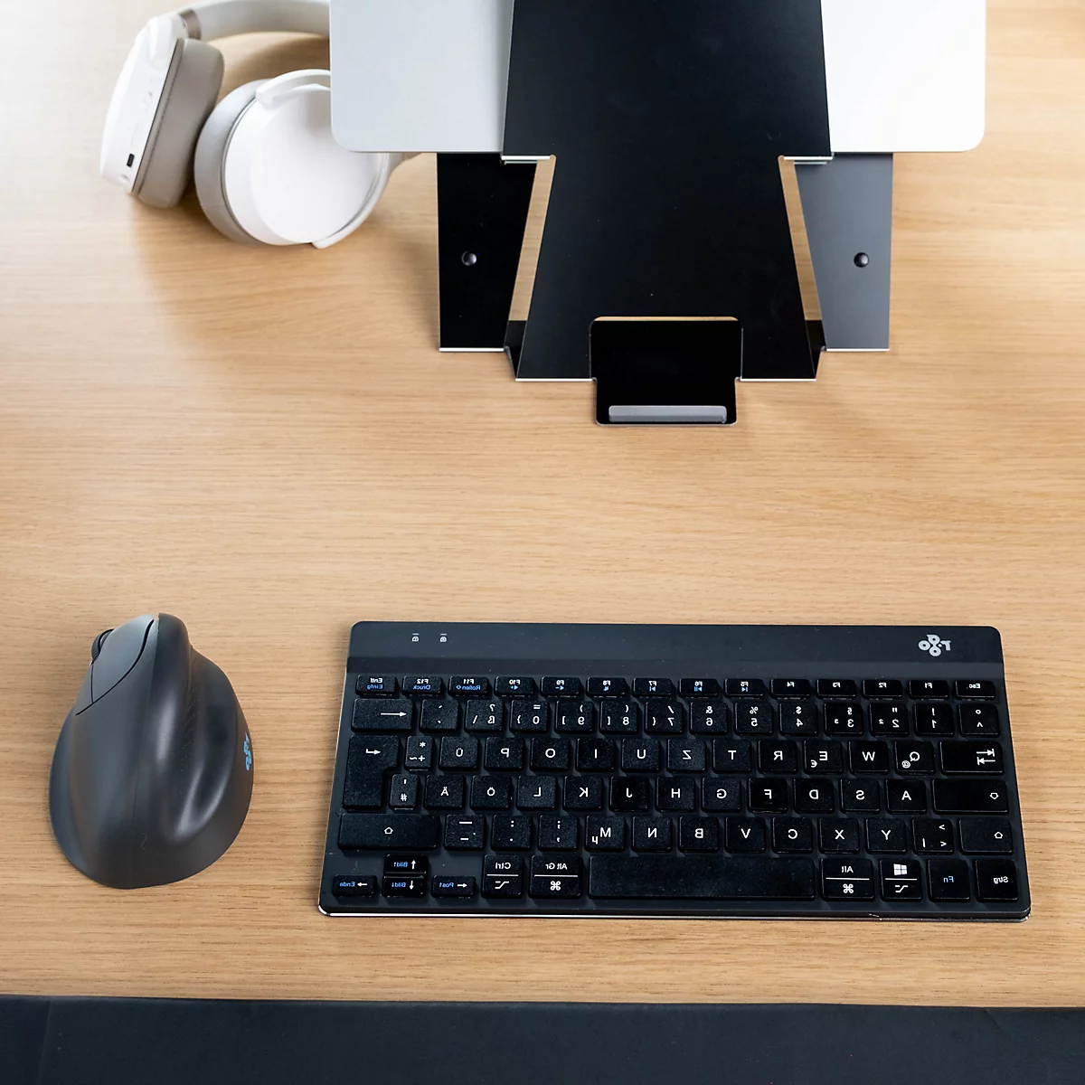 Blick von oben auf einen Schreibtisch mit schwarzem Ständer für ein Tablet, Kopfhörern, einer vertikalen Maus und einer Tastatur.