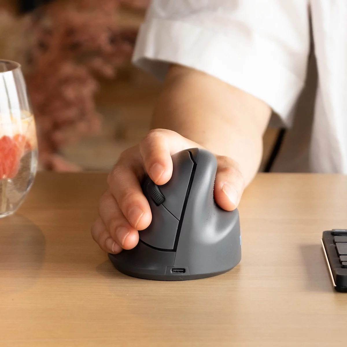 Eine Hand bedient eine ergonomische vertikale Computermaus auf einem hellen Holztisch.