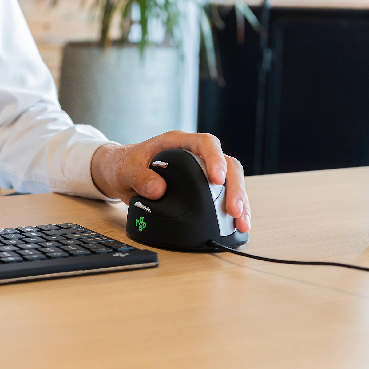 Eine Person benutzt eine vertikale Maus. Der Arm liegt auf dem Tisch, die Hand umfasst die ergonomische Maus.