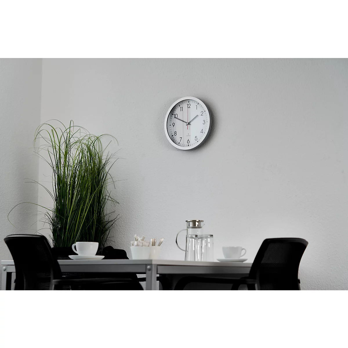 White clock on grey wall, table with teacups and decor.