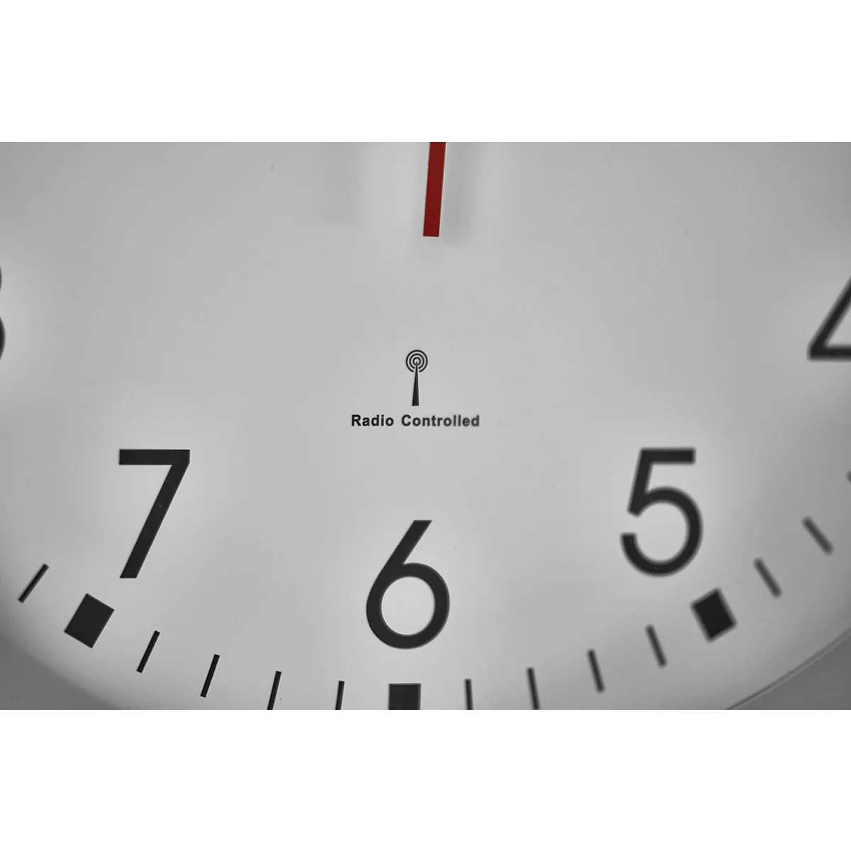 Close-up of a white radio clock, red hands, black numbers, radio symbol and lettering.