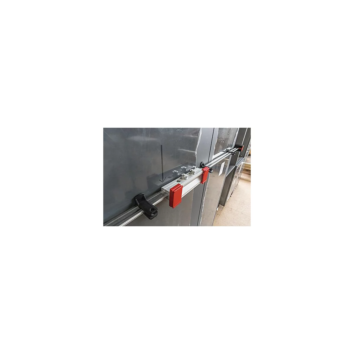 Gros plan d'une structure métallique avec des rails, des pinces et des accents rouges. Une flèche noire pointe vers une ligne sur la surface.