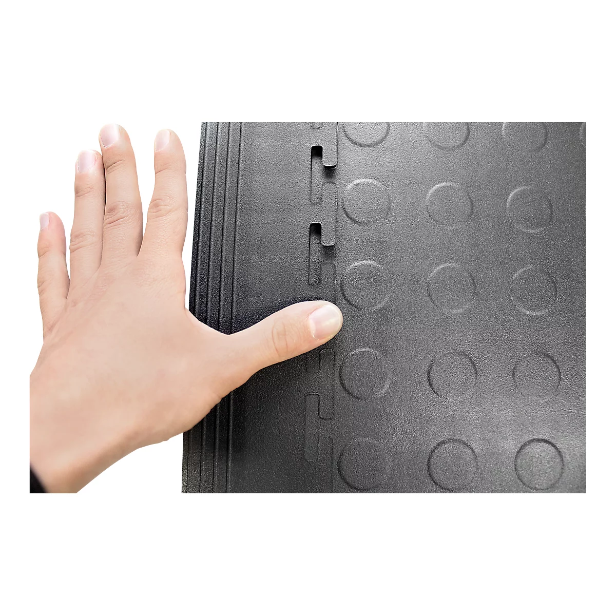 Helle Hand berührt schwarze, ineinandergreifende Bodenplatten mit Kreismuster und Verbindungsstücken.