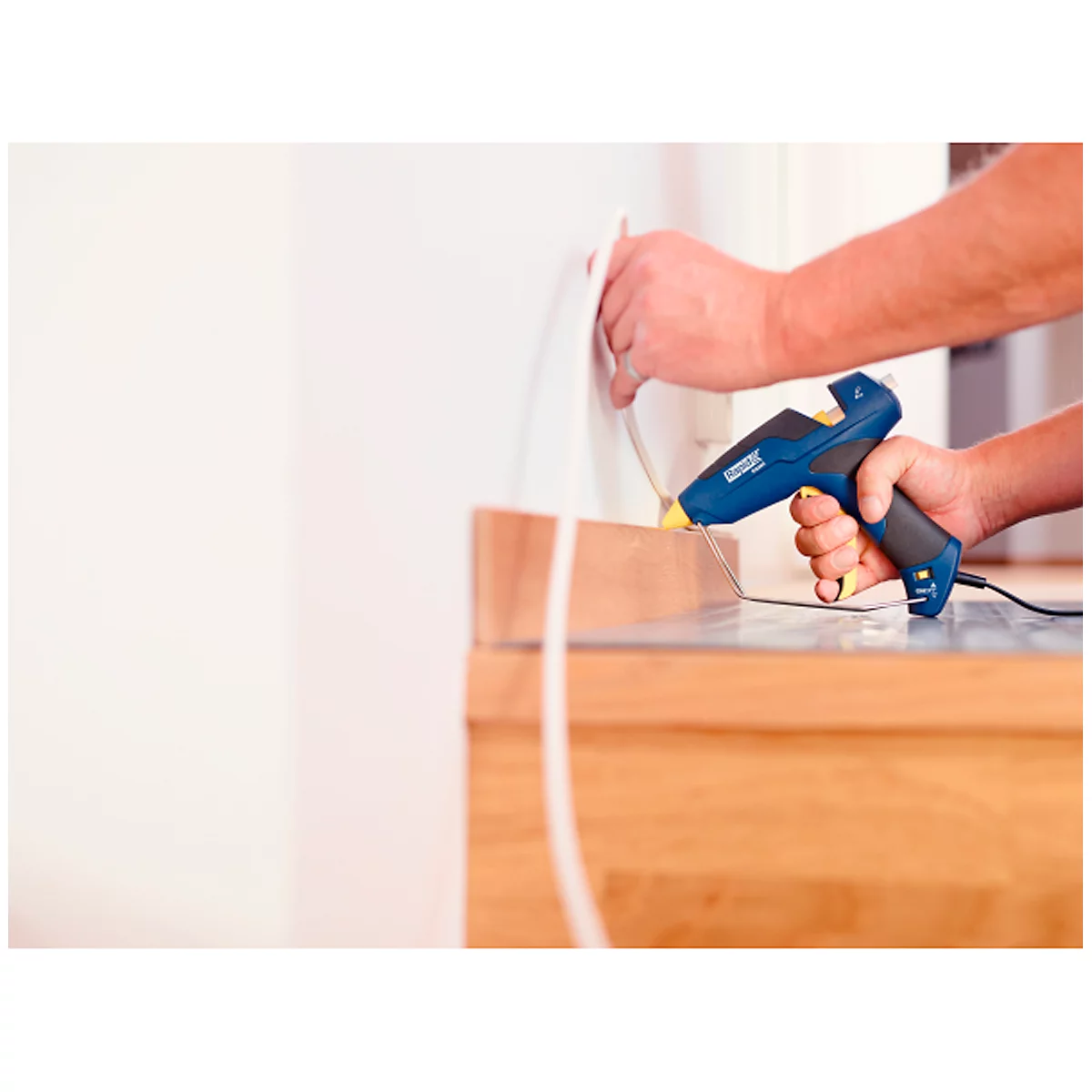 A person is using a blue hot glue gun to attach wood to a wall.