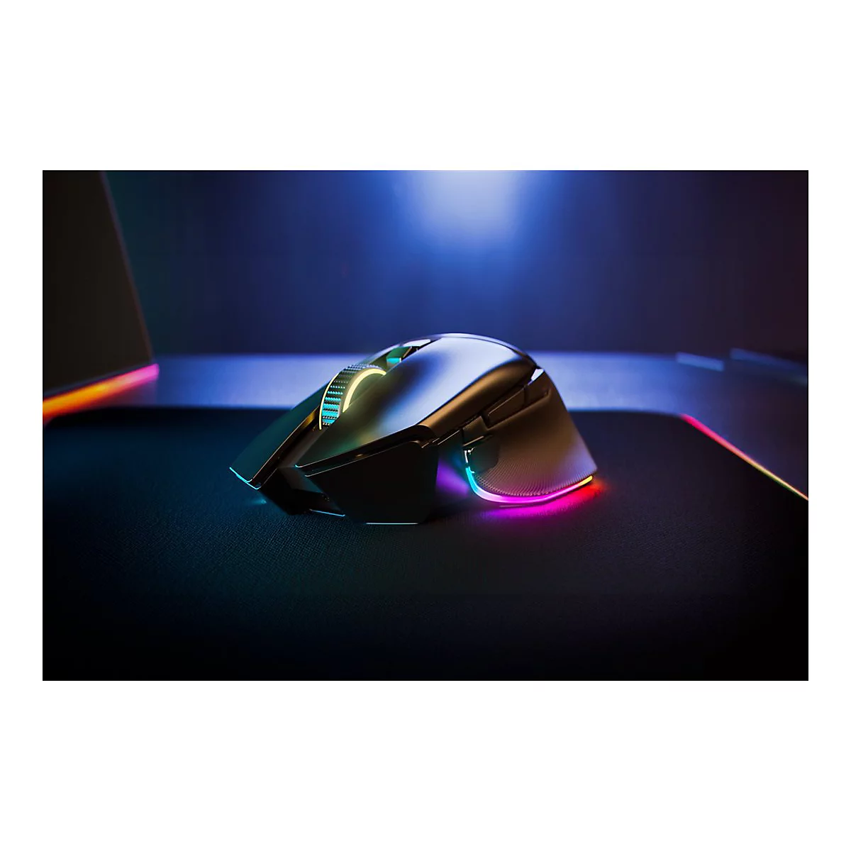 Drahtlose Gaming-Maus mit RGB-Beleuchtung auf schwarzem Mauspad, farbige Lichter. Im Hintergrund ein Laptop.