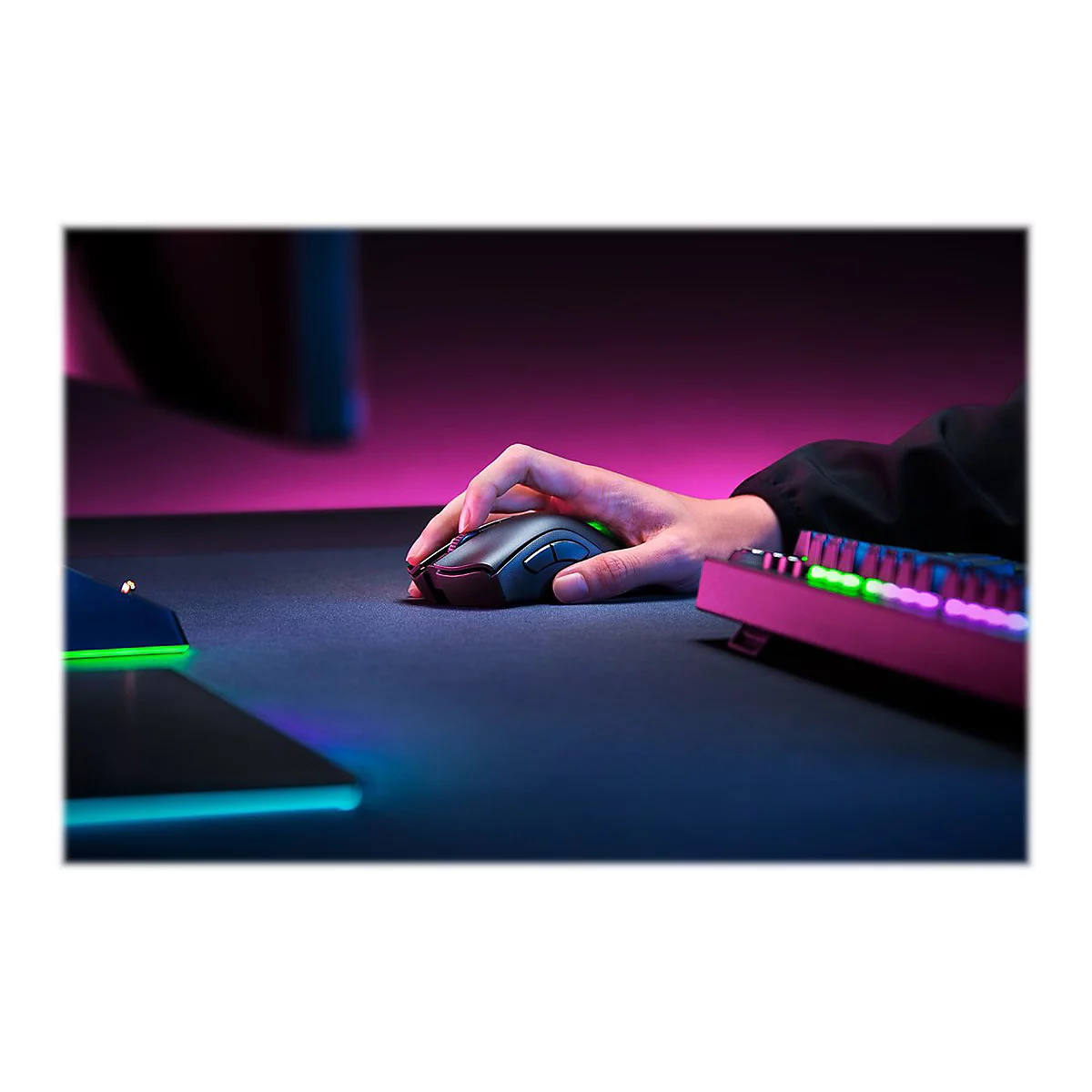 Person bedient eine graue Maus, neben einer pinkfarbenen Tastatur. Das Szenario ist in blau-pinkes Licht getaucht.