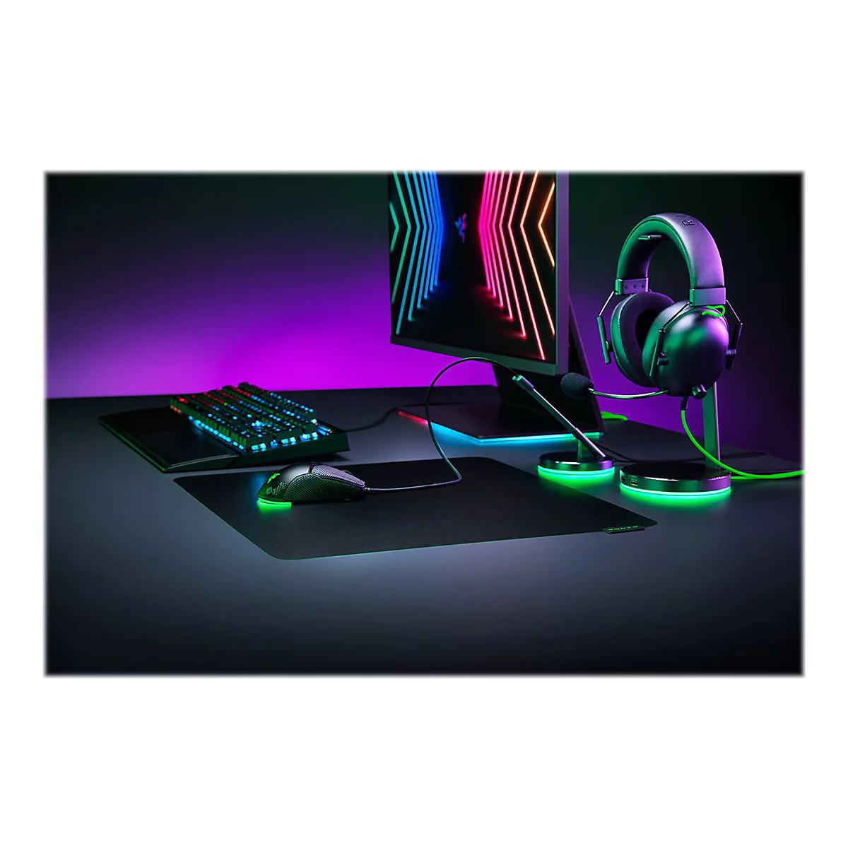 Gaming-Set mit Tastatur, Maus, Mikrofon und Headset auf einem Schreibtisch in buntem Neonlicht.