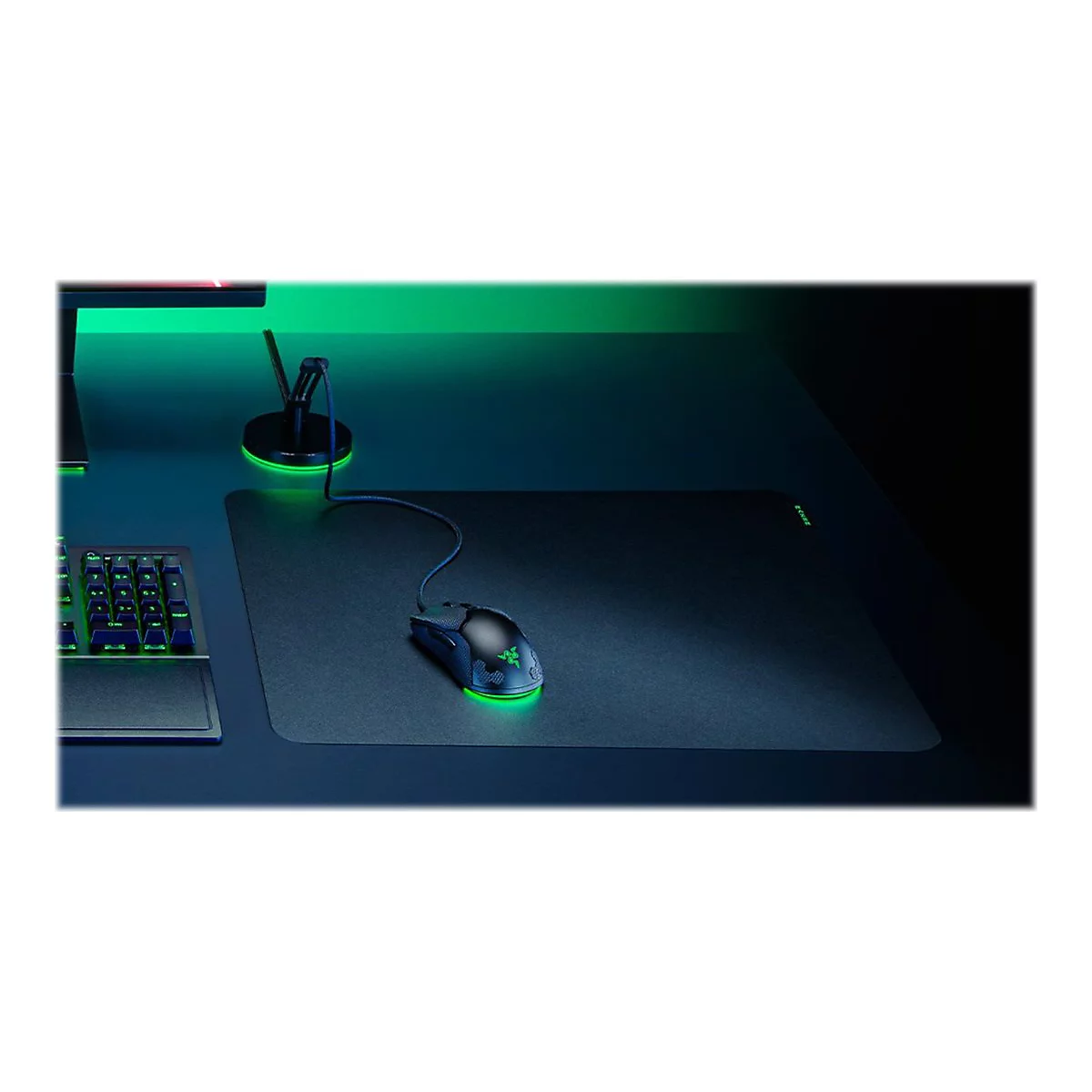 Gaming-Maus mit grün leuchtender Unterbodenbeleuchtung auf einem Mauspad, daneben eine Tastatur und ein Kabelhalter.