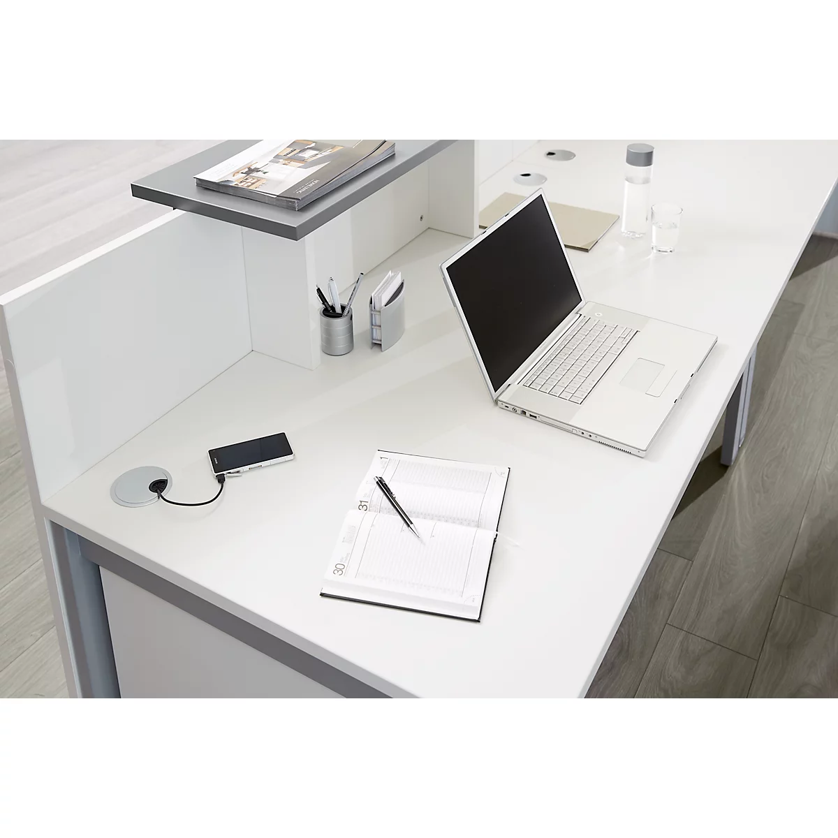White desk with laptop, notebook, pen, mobile phone, and office supplies.