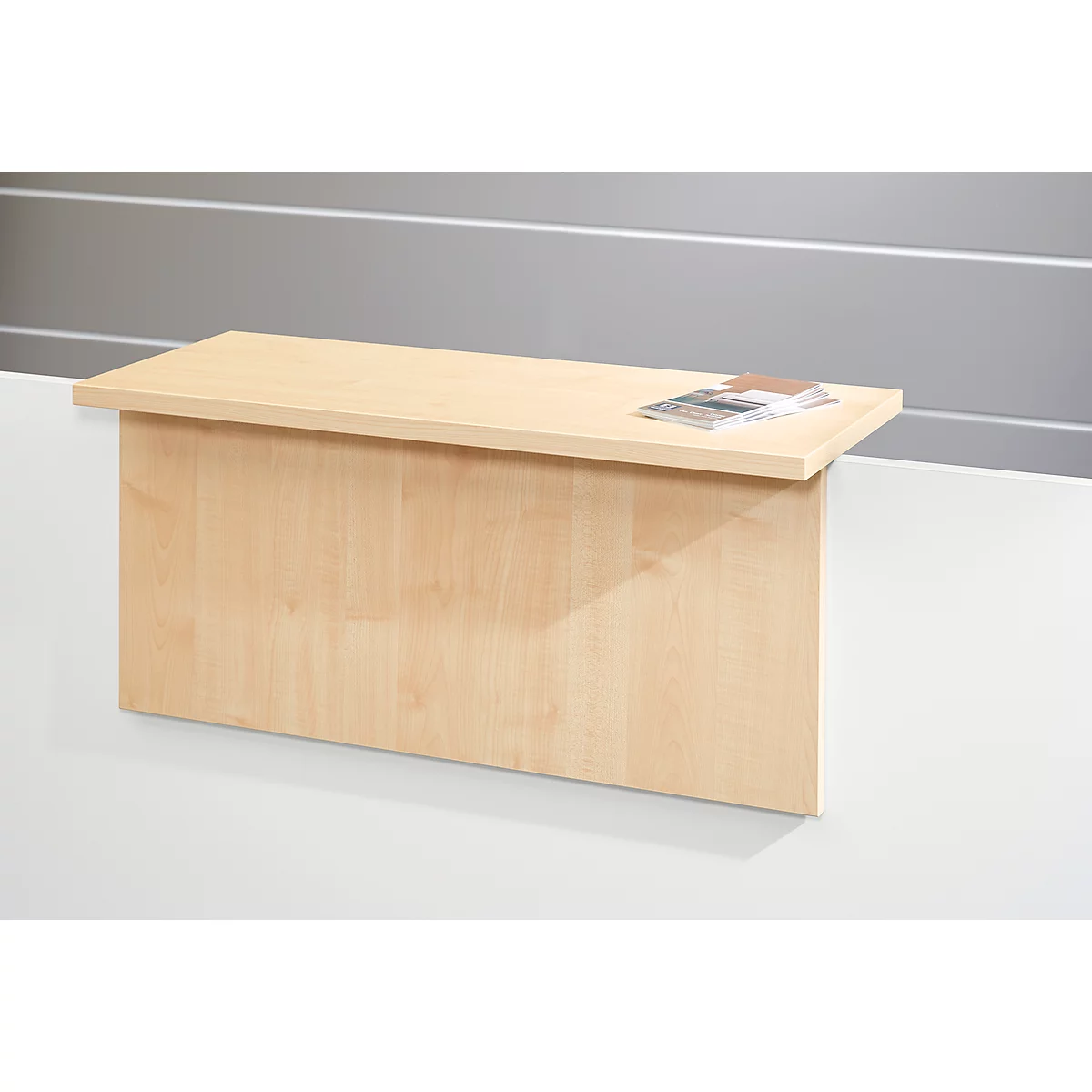 Light brown, rectangular reception counter with a slightly overhanging top. Flyers are on the counter. Background is gray-white.