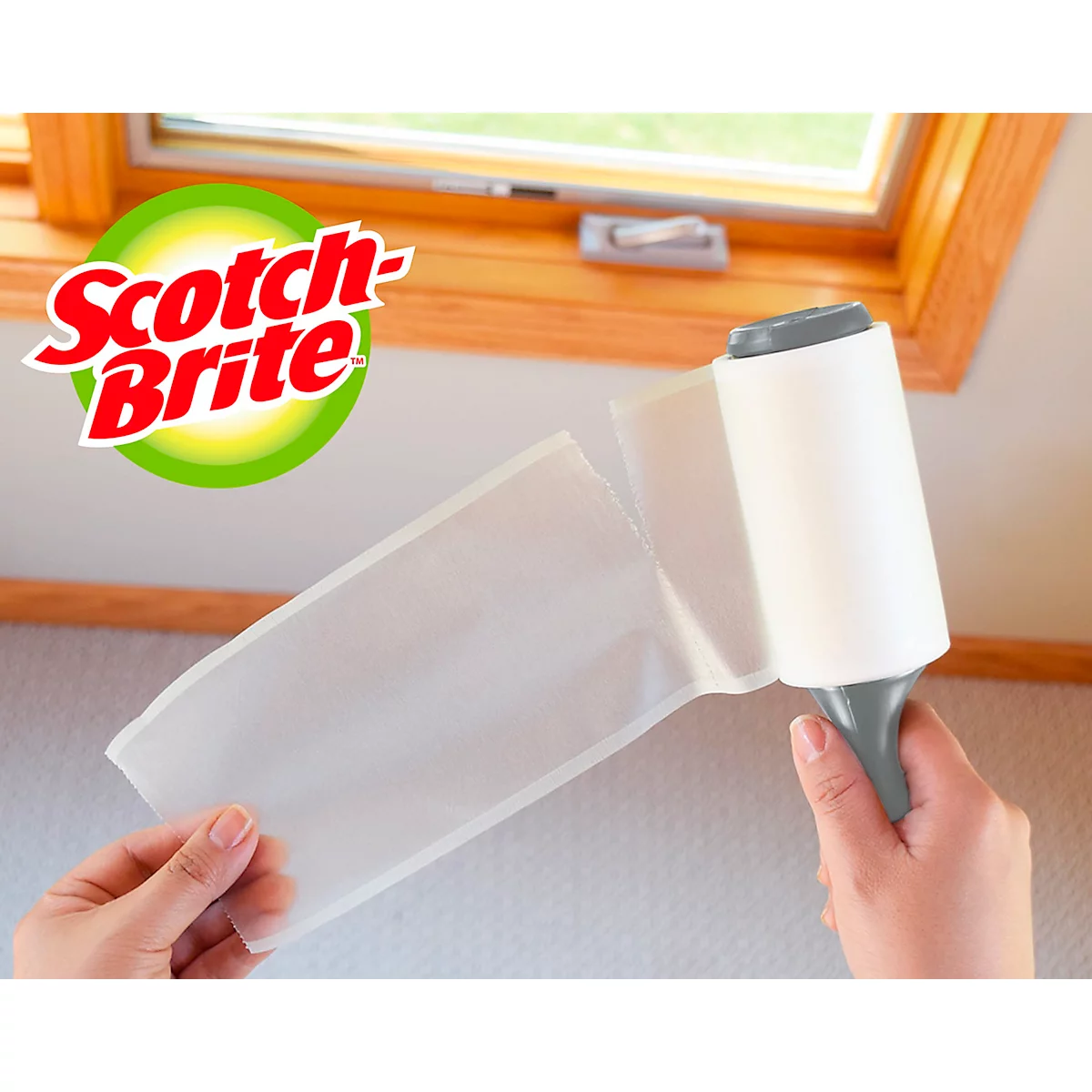 Mains tenant un rouleau anti-peluches Scotch-Brite avec une fenêtre en arrière-plan.