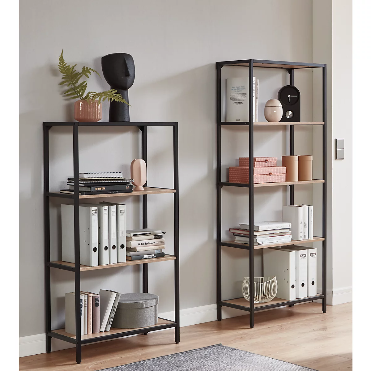 Zwei schwarze Metallregale mit Holzablagen, gefüllt mit Büchern, Ordnern und Dekorationsartikeln.