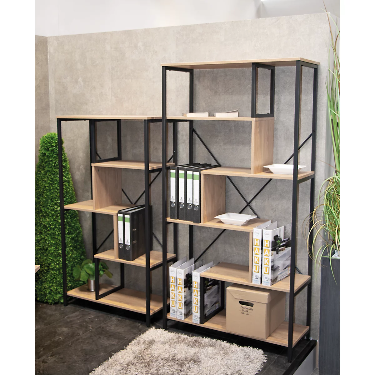 Zwei Holzregale mit schwarzen Metallrahmen. Auf den Regalen stehen Ordner, Bücher und Deko-Elemente.