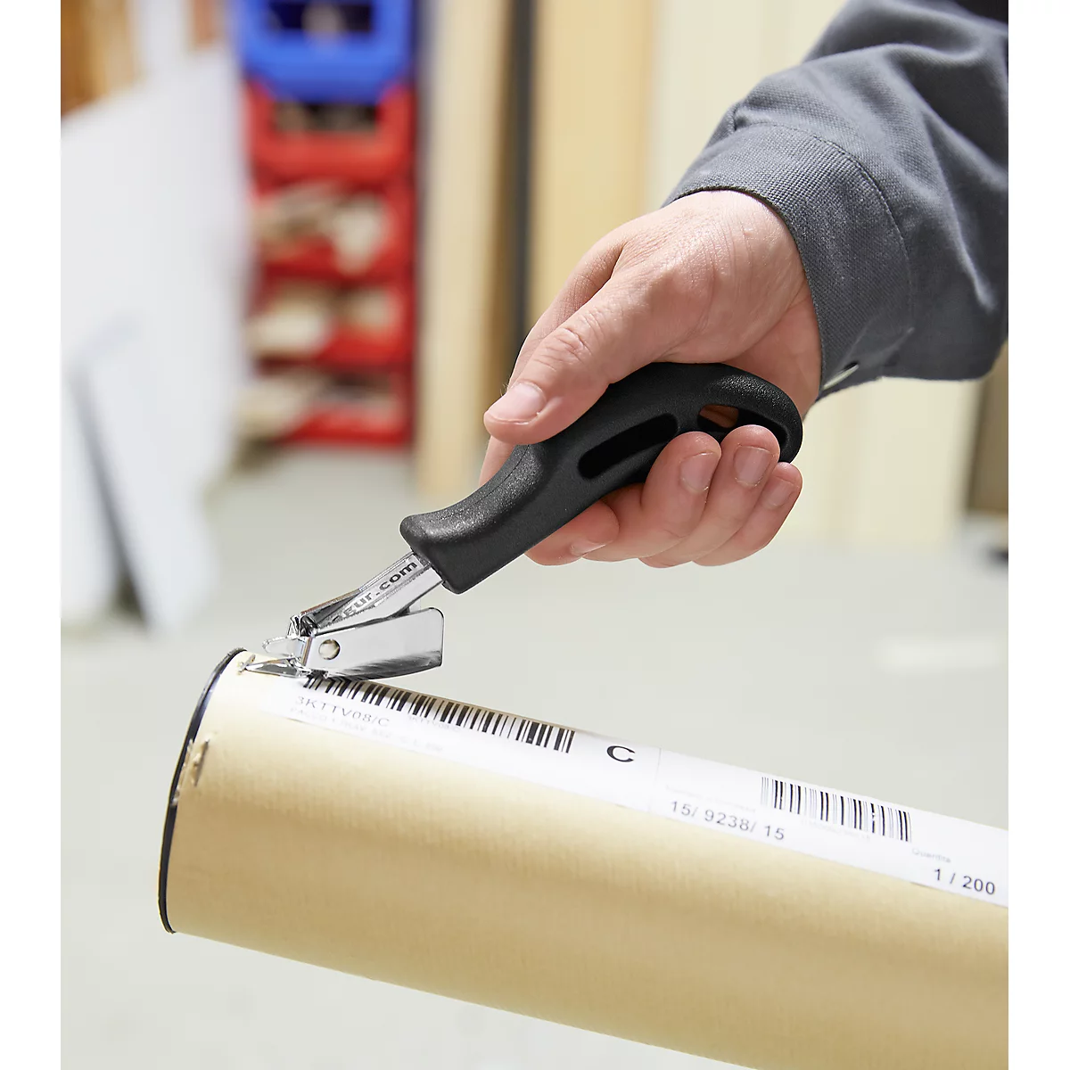 Person is cutting a paper tube with a special tool. Black handle, silver tool, paper with barcode.