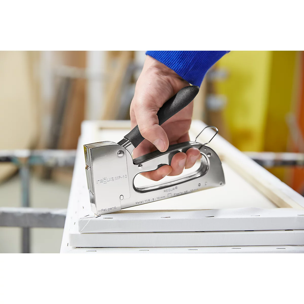 A person using a silver staple gun to attach canvas to a wooden frame.