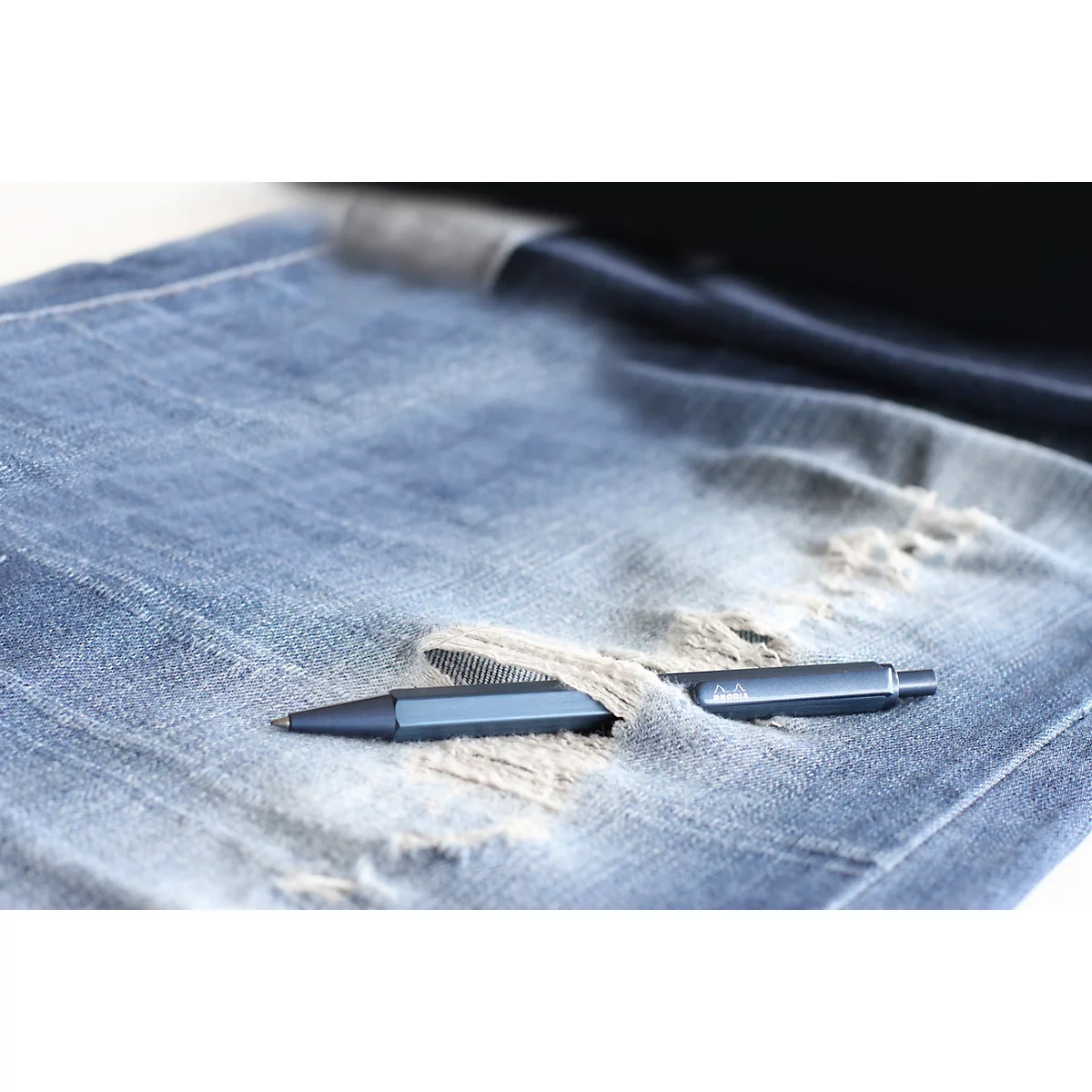Blauer Stift in einer Jeans-Hosentasche mit abgenutzten Löchern, auf hellem Hintergrund. Nahaufnahme.