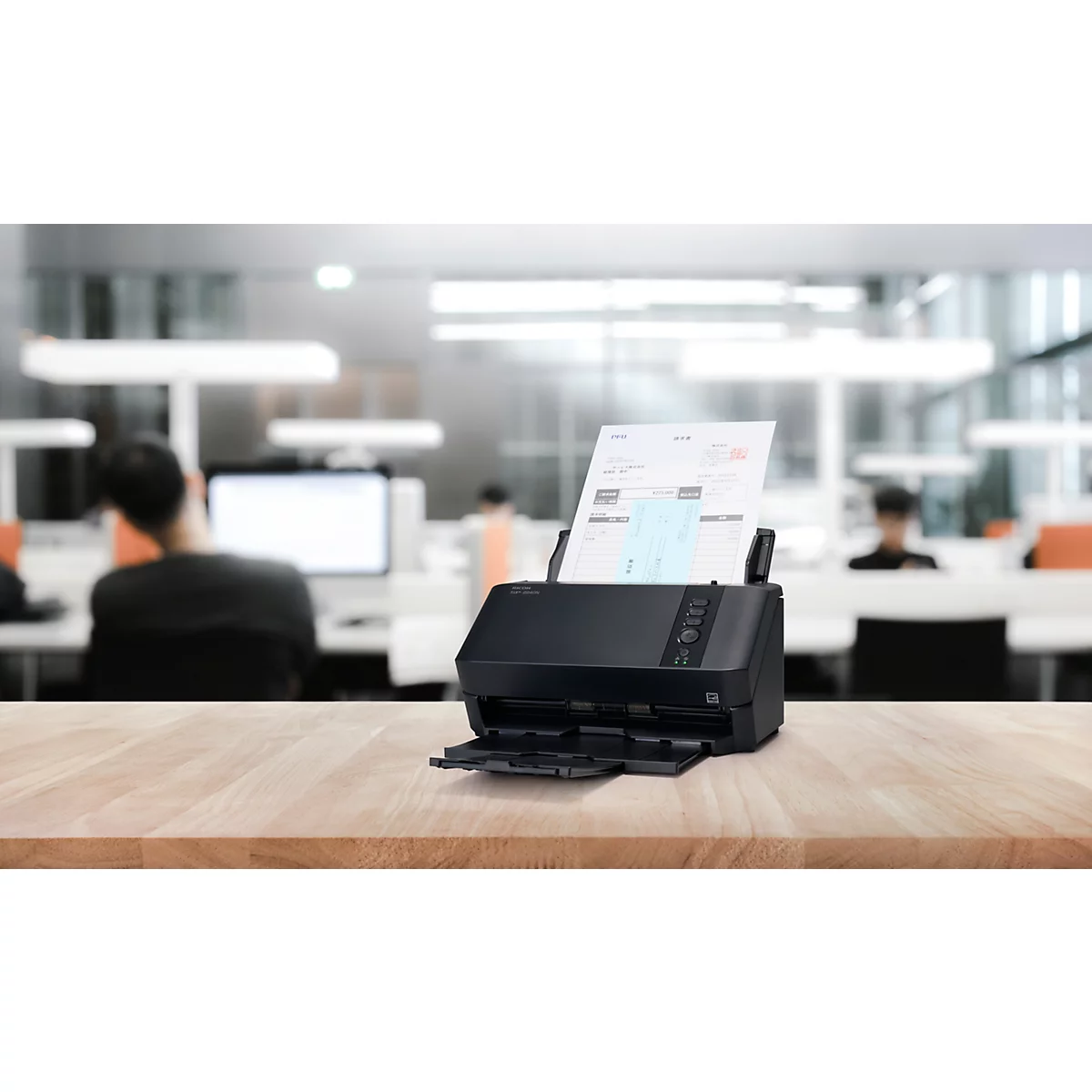 Schwarzer Dokumentenscanner auf einem Holztisch in einem verschwommenen Büro.