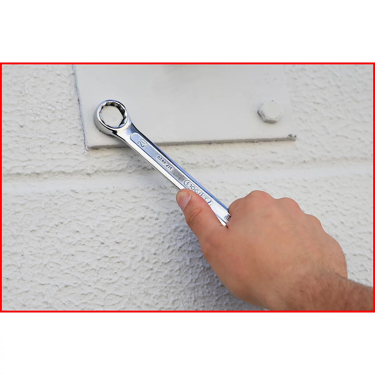 Eine Hand hält einen Schraubenschlüssel, um eine Schraube zu lösen. Der Schraubenschlüssel liegt auf einem weißen Untergrund.