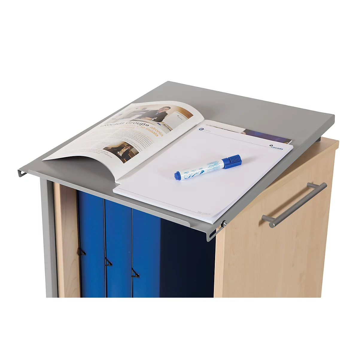 Armoire brun clair avec intérieur bleu. Dessus, un magazine ouvert, un presse-papiers, un stylo et un feutre bleu.