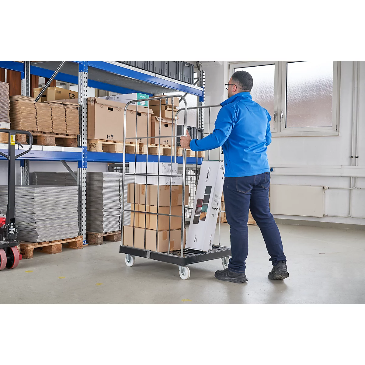 Een man duwt een kar vol dozen en promotiemateriaal in een magazijn. Schappen met goederen op de achtergrond.