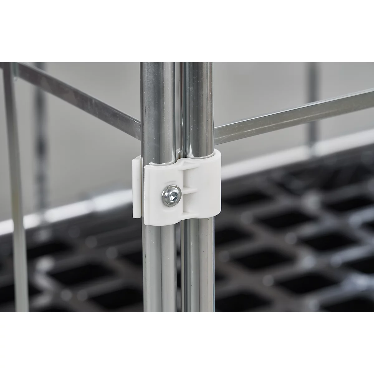 Detailopname van een metalen buisframe met witte kunststof connector en schroef.