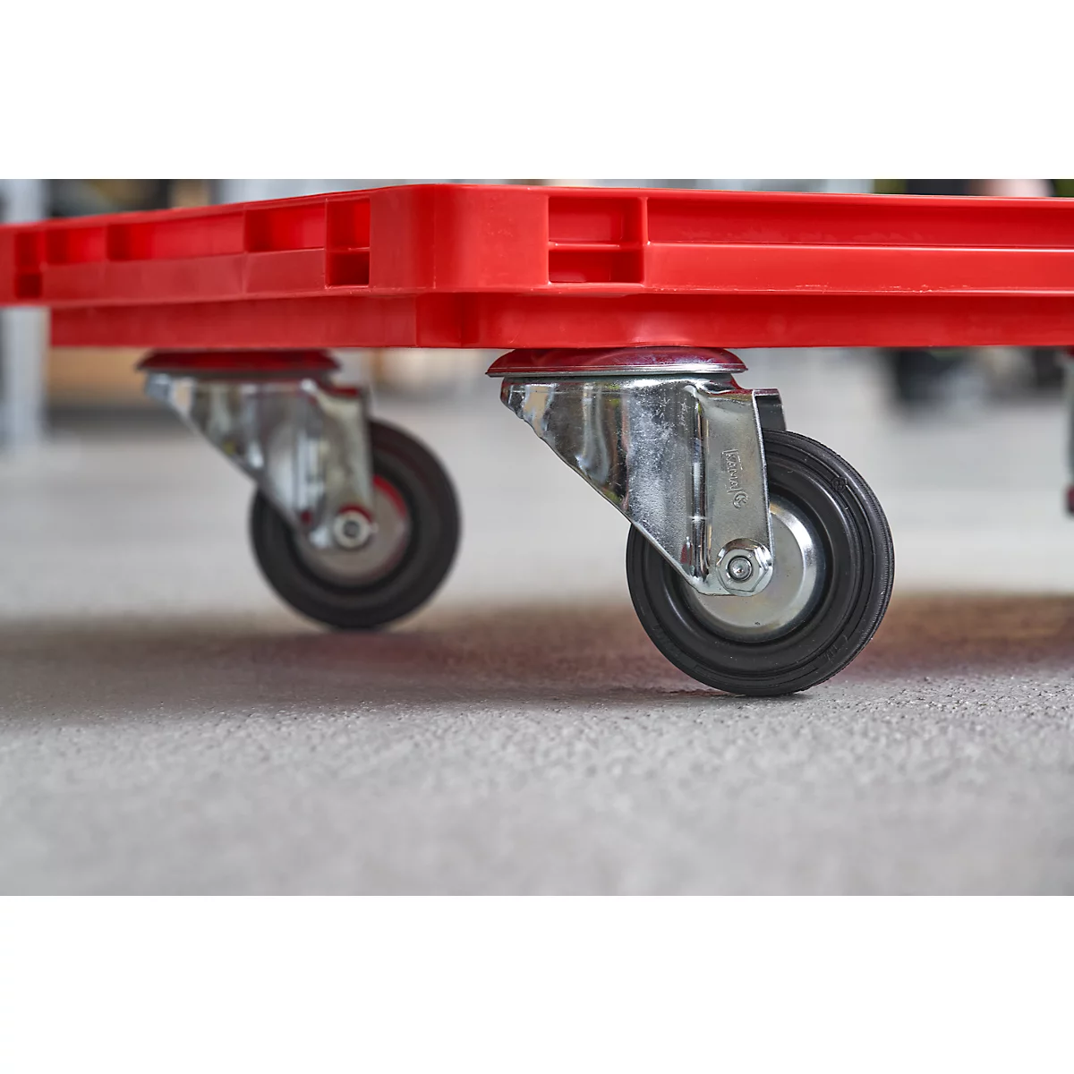 Close-up of two wheels under a red plastic container. The wheels are black with silver mounts.