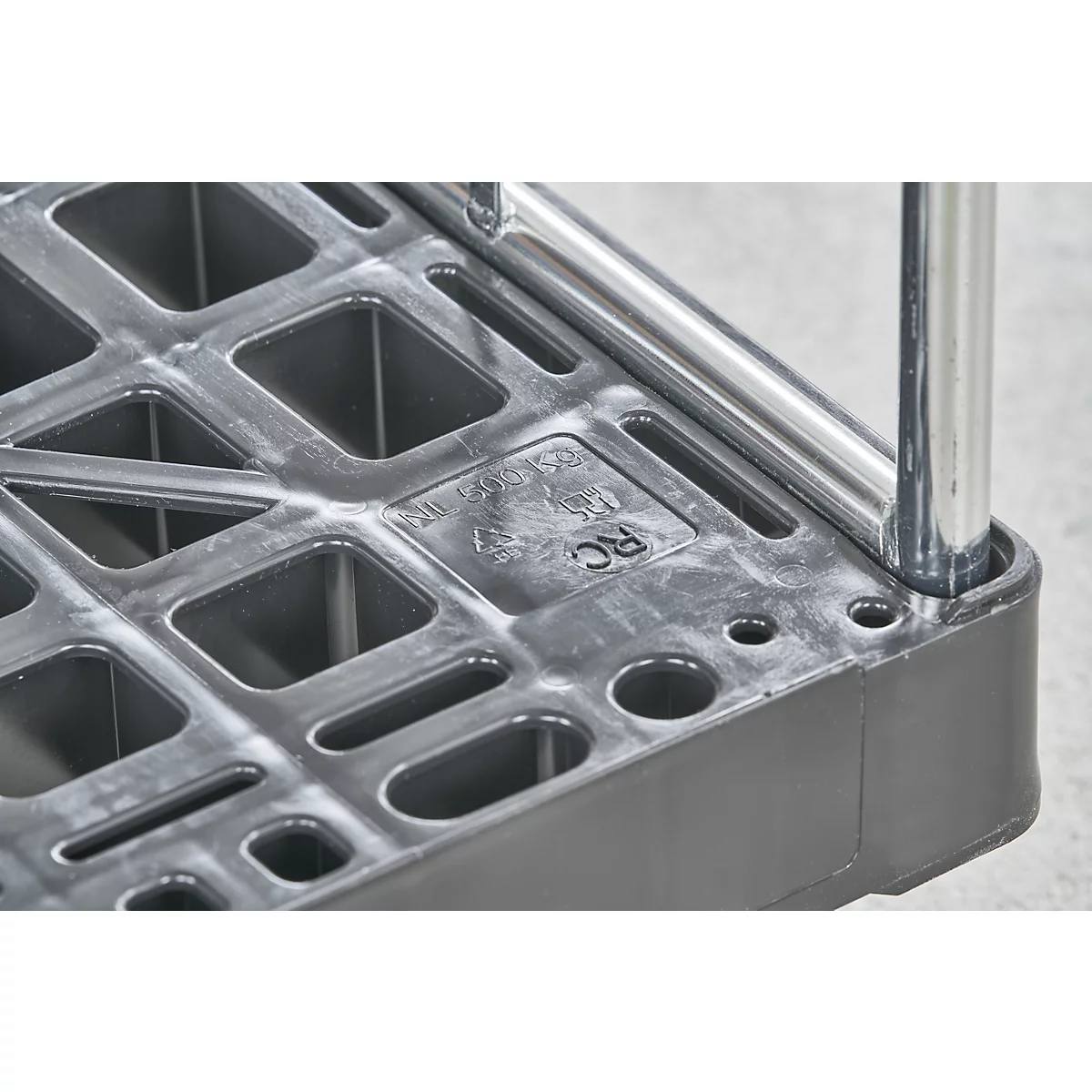 Gros plan sur une surface en plastique gris avec des découpes carrées. Un cadre en métal chromé est partiellement visible.