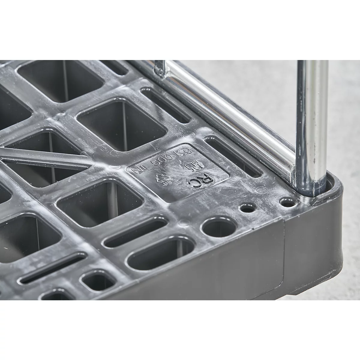 Gros plan d'un chariot en plastique noir avec des trous carrés et une rampe en métal. Lettres RC visibles.