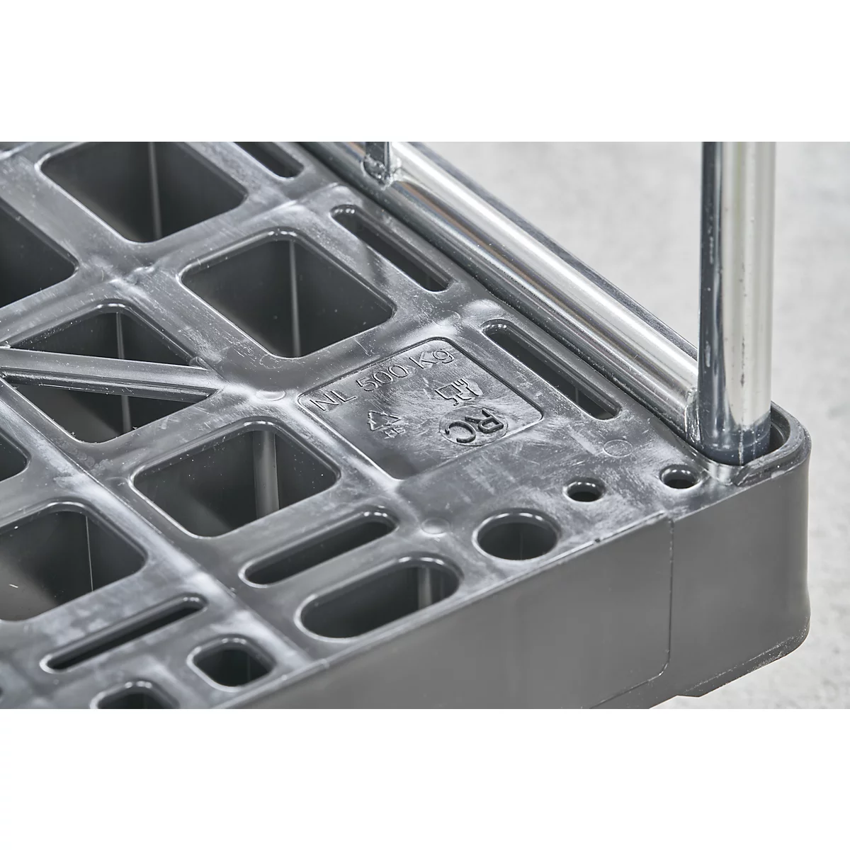 Detailaufnahme einer Ecke eines schwarzen Kunststoff-Rollwagens mit quadratischen Aussparungen und verchromten Metallstangen.