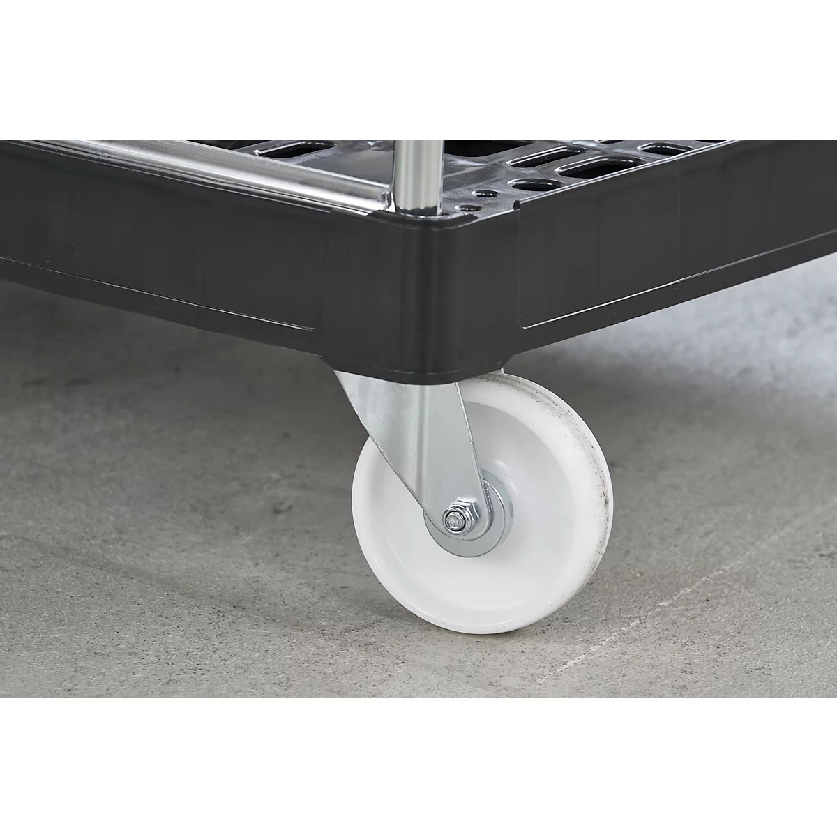 Detailaufnahme eines weißen Rollrads an einem schwarzen Einkaufswagen, der auf grauem Boden steht.