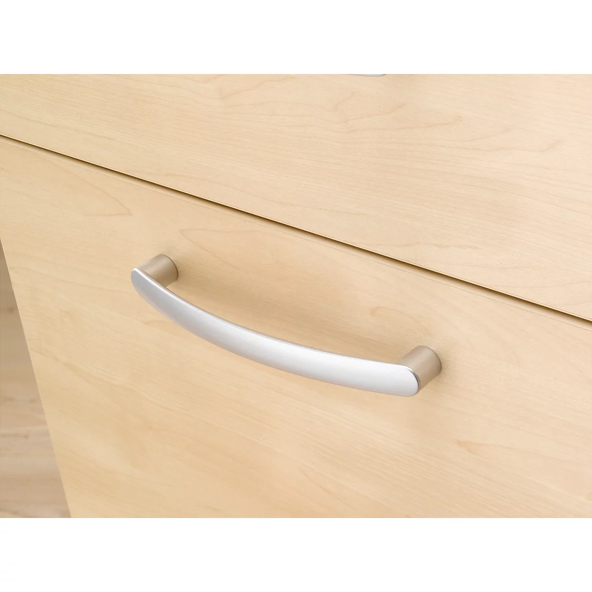 Nahaufnahme einer hellen Holzschublade mit einem silbernen, gebogenen Metallgriff.