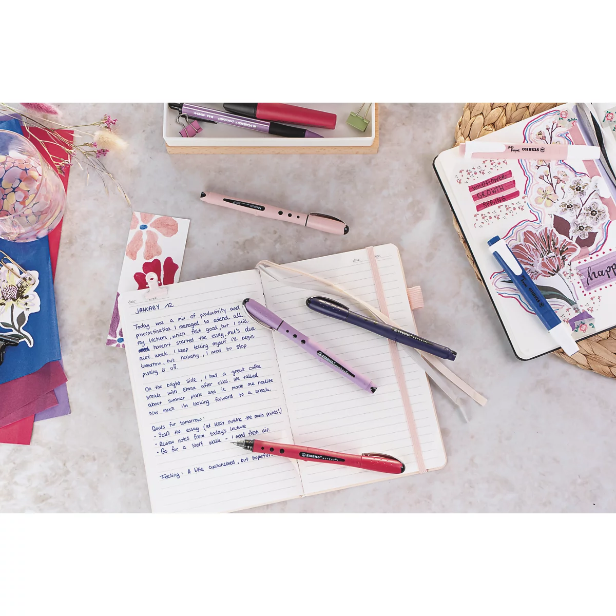 Gros plan sur des stylos et des cahiers. Cahier ouvert avec des notes manuscrites, des stylos colorés et des éléments décoratifs.