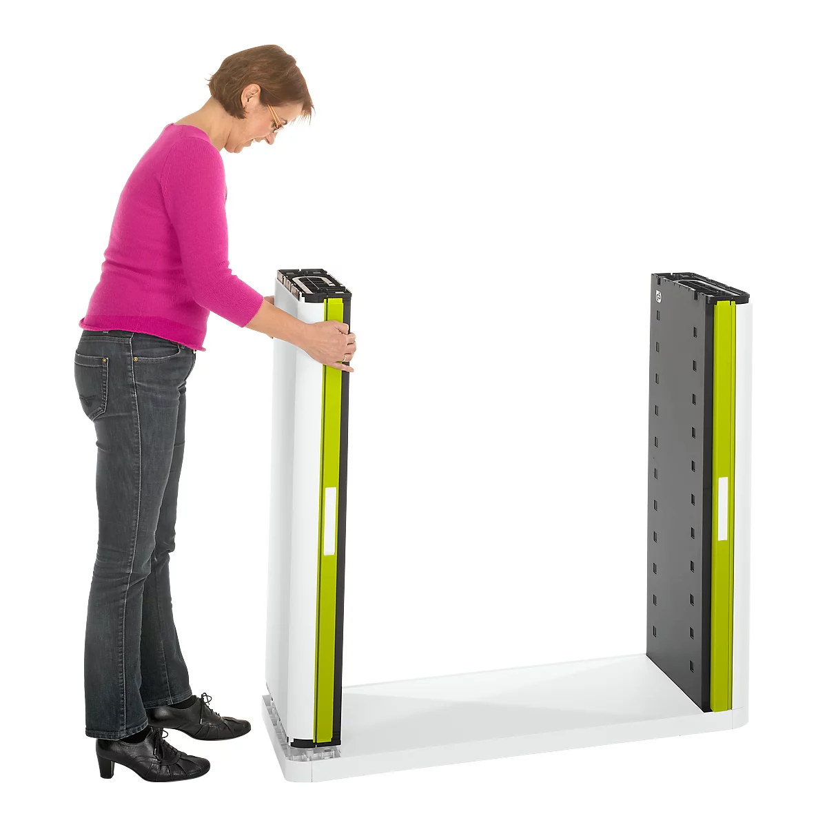 A woman is setting up an element of a white shelf. The shelf has green accents and stands on a white floor. The woman is wearing a pink shirt.