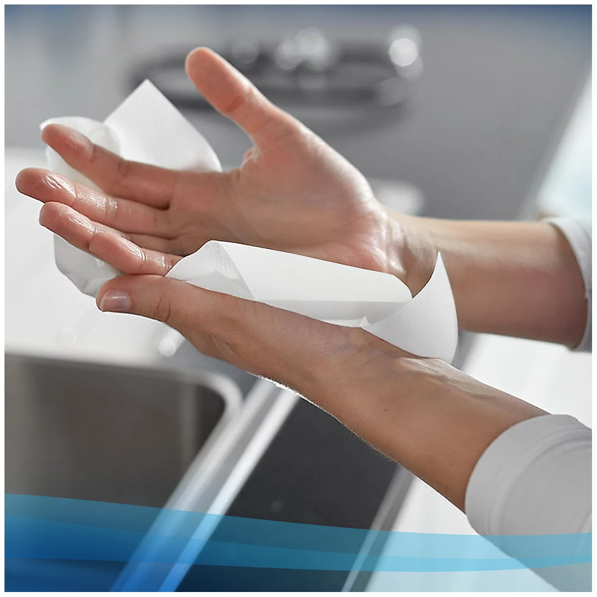 Manos secándose con una toalla de papel blanca. Se puede ver un fregadero en el fondo.