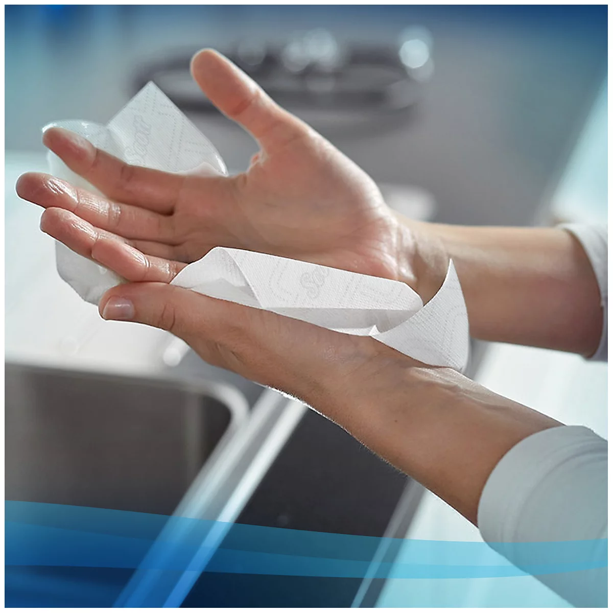 Manos secándose con una toalla de papel blanca. Un fregadero es visible en el fondo.