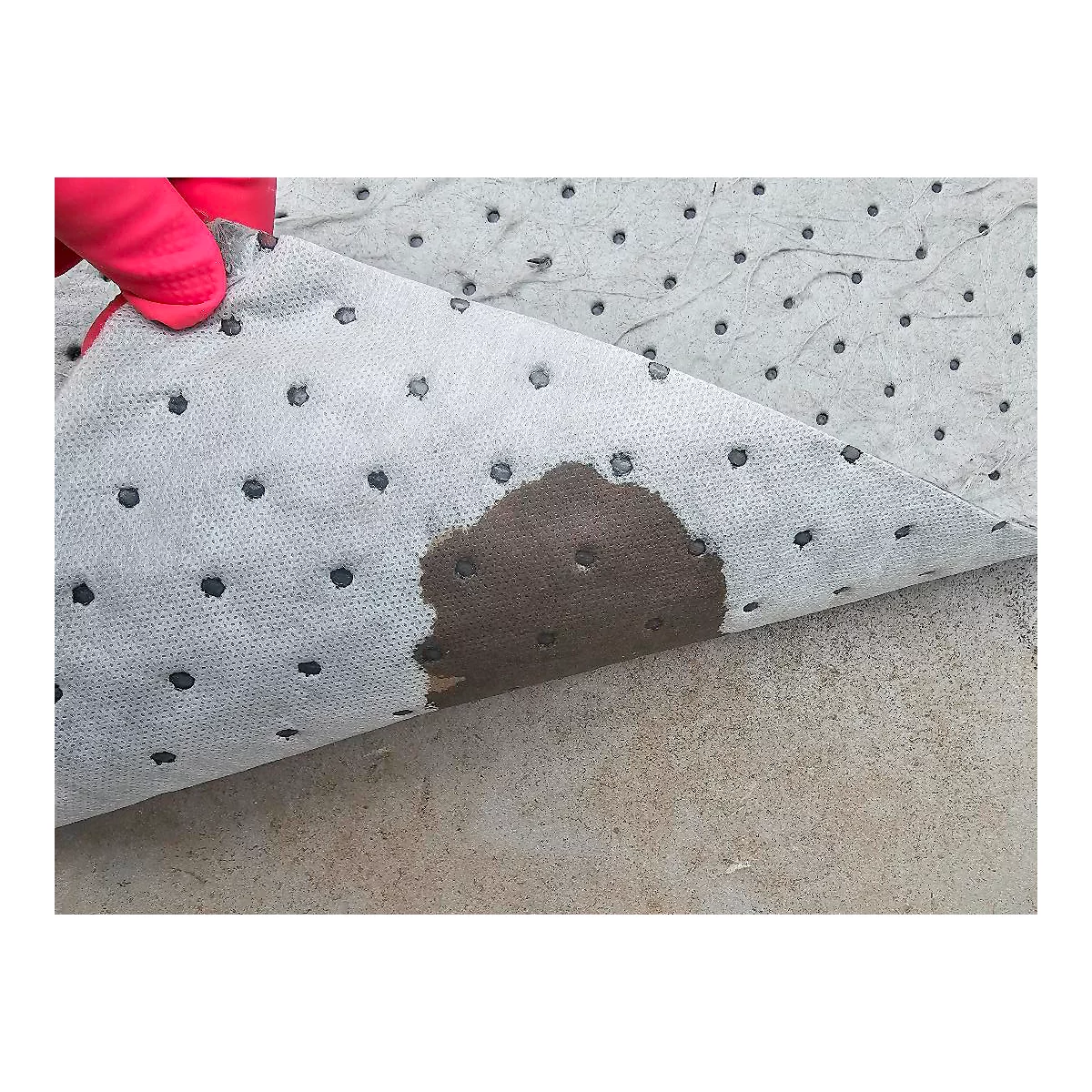 Vellón absorbente gris, cubierto de líquido oscuro. Una mano con un guante rojo levanta el vellón.