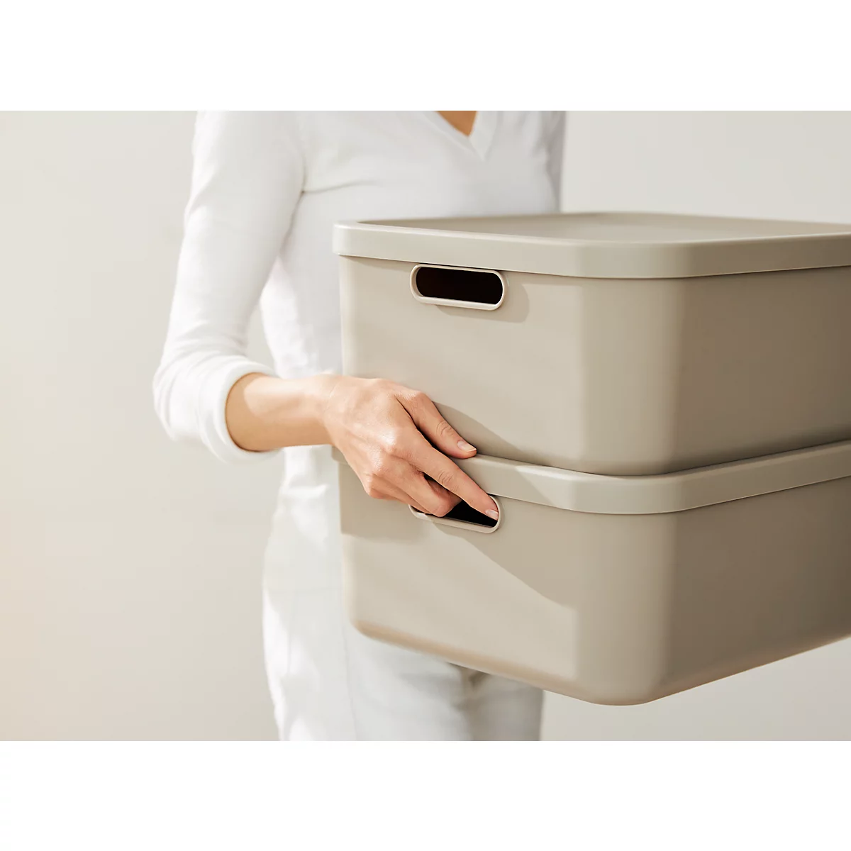 Person holding two beige storage boxes. The boxes are stacked on top of each other and have recessed handles.